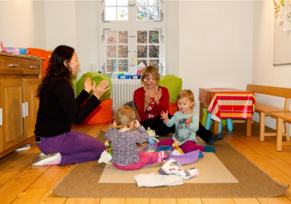 Zwei Kleinkinder beim Spielen mit der Betreuerin und einer Mutter